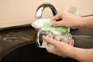Persona che lava bicchiere nel lavandino con spugna e sapone