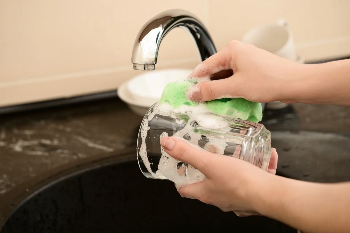 Persona che lava bicchiere nel lavandino con spugna e sapone