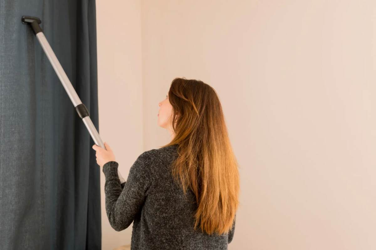 Donna che pulisce le tende con l'aspirapolvere