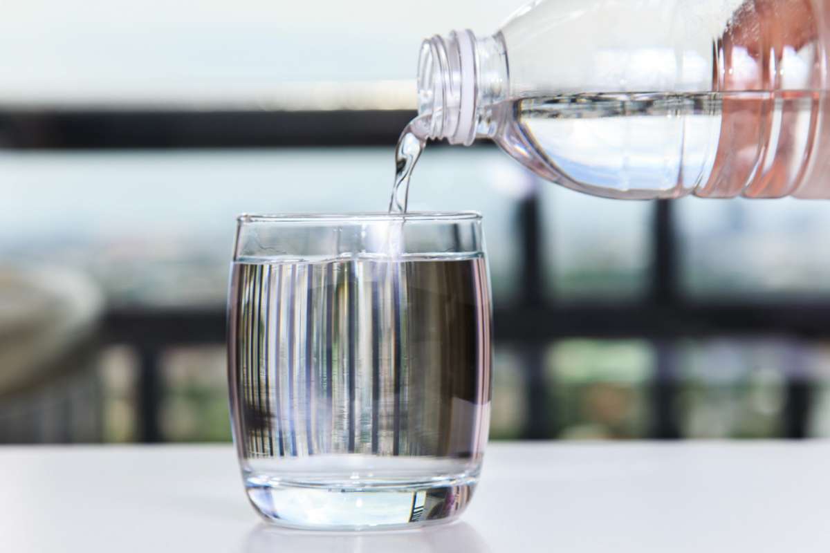 Persona che versa acqua in un bicchiere pulito